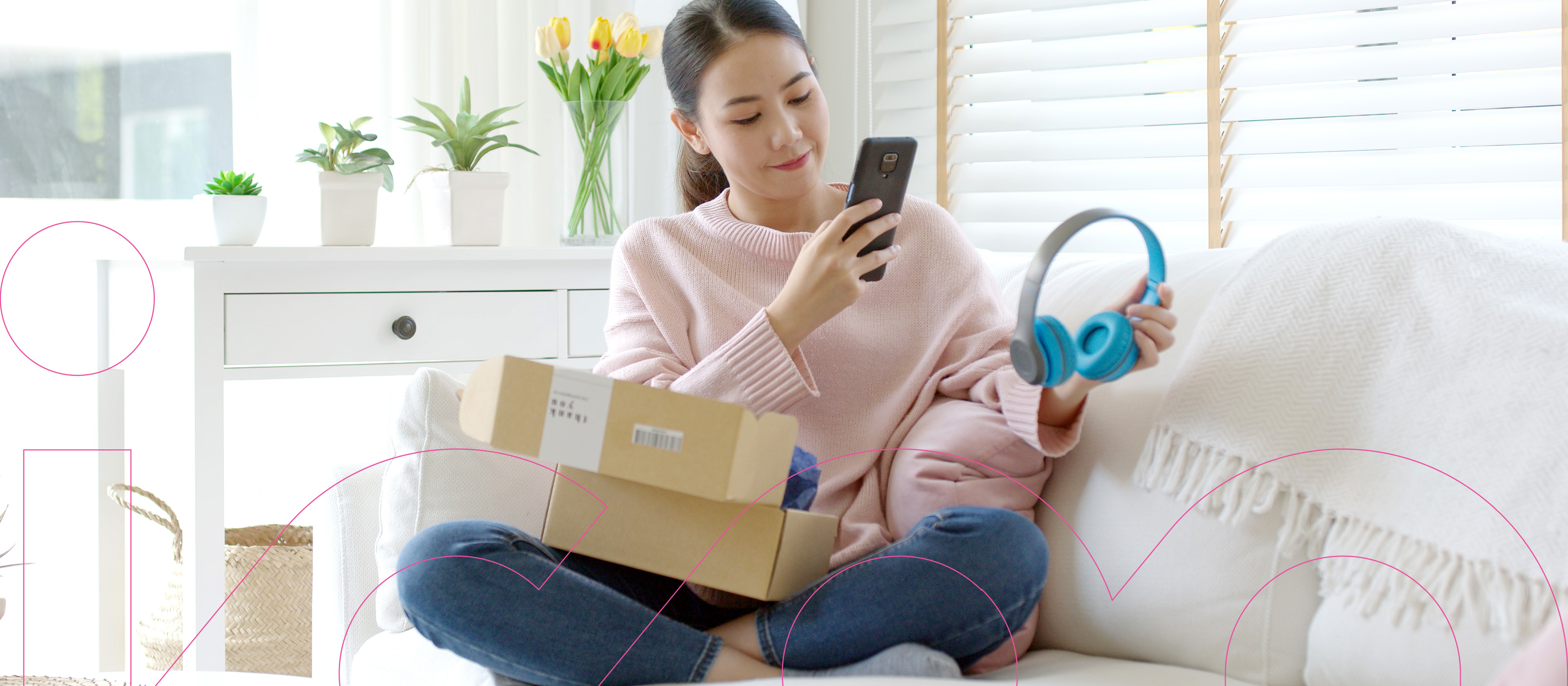 A young woman has taken headphones out of a box in her lap and is photographing it with her phone to use in an online review